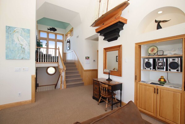 A room with a desk, chair, and a bookshelf with speakers. There is a staircase leading to another level.