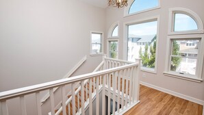 Ein geräumiger Raum mit Holzboden, weißen Wänden und einer weißen Geländer. Große Fenster mit Rundbögen lassen natürliches Licht herein.