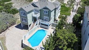 Une maison à deux étages avec une piscine, située près d’une plage et dotée d’une promenade en bois.