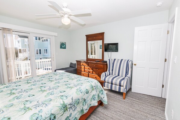 A bedroom with a bed, a dresser, a chair, a ceiling fan, a TV, and a door.