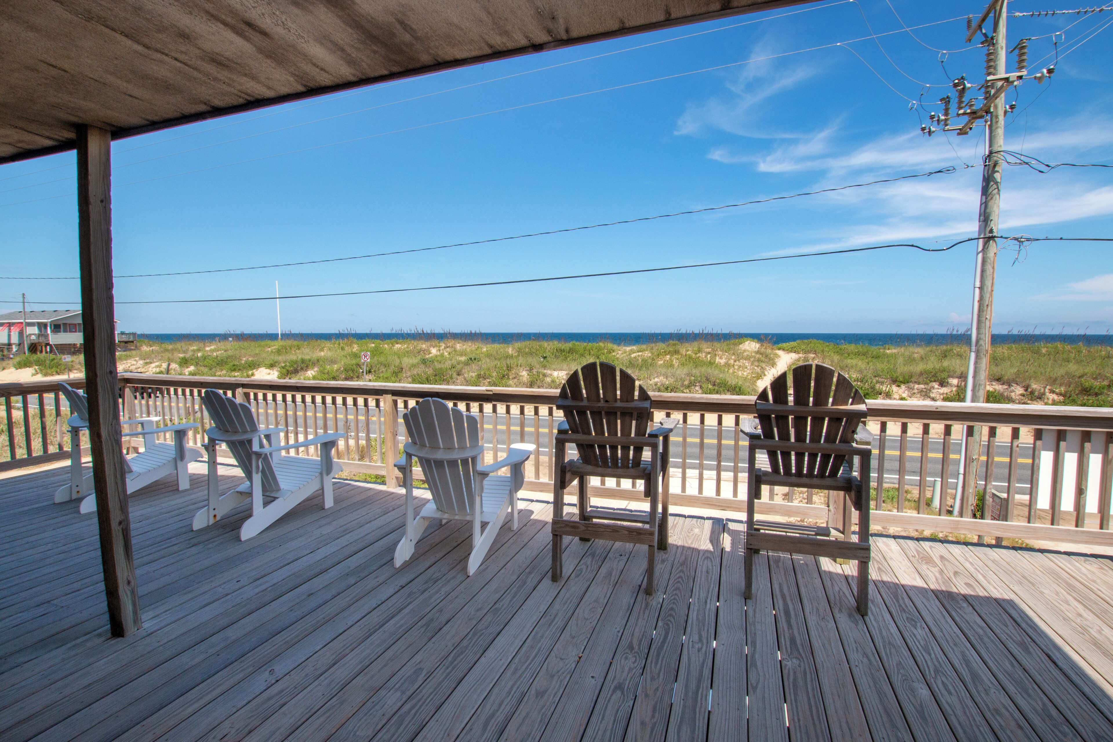 A wooden deck with three Adirondack chairs facing a beach.