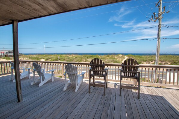 A wooden deck with three Adirondack chairs facing a beach.