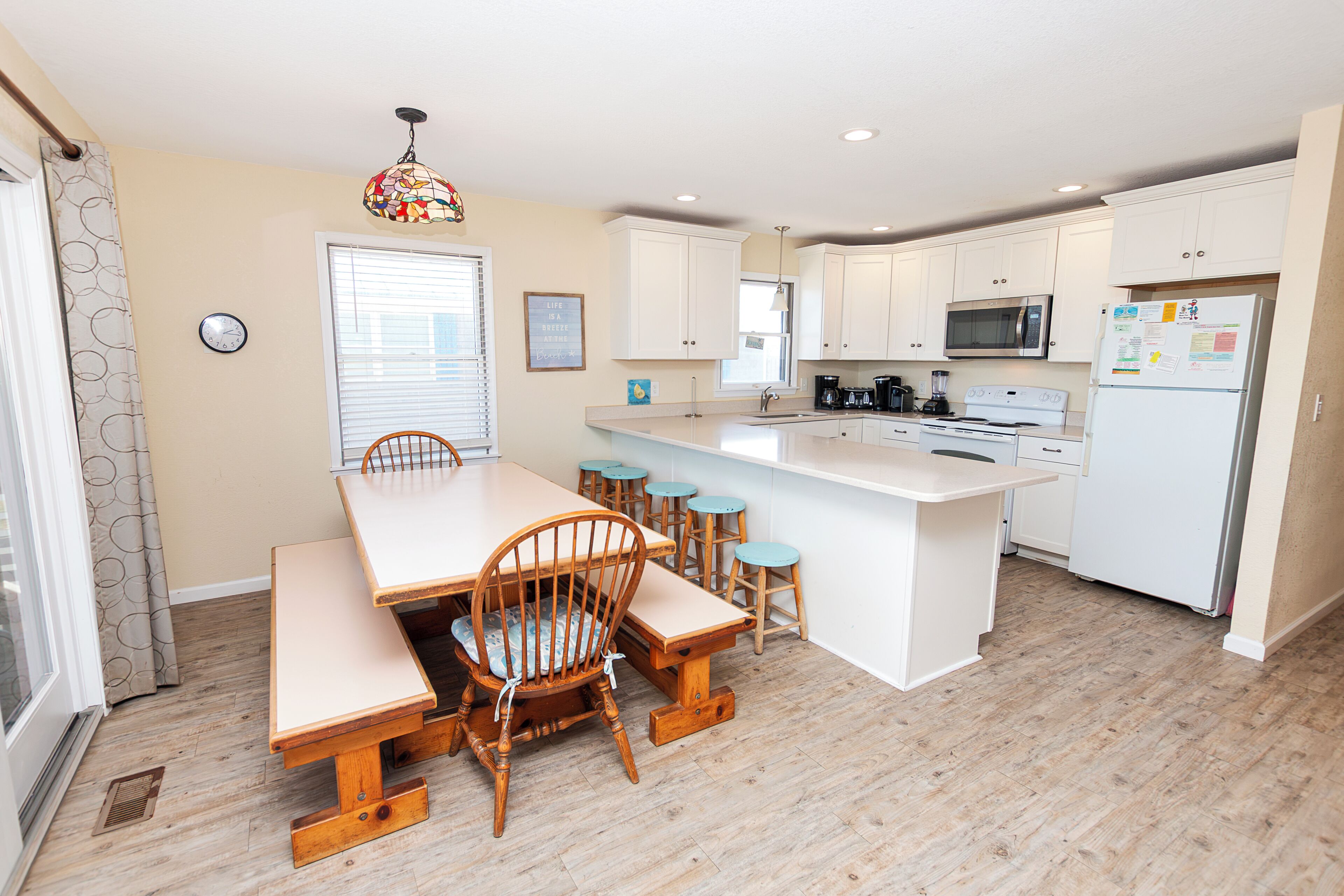 A modern kitchen with white cabinets, a central island with stools, a microwave, and a refrigerator.