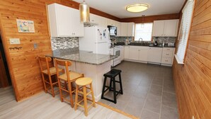 A compact kitchen with wooden walls, a granite countertop, white cabinets, and a small bar area with stools. - Oceanside, Private Pool, Sun Deck, Hot Tub, OS3N, The Lone Star Fish (Corolla)