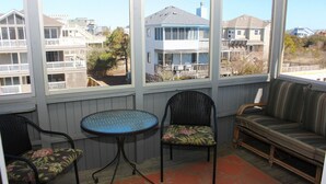 A sunroom with a view of neighboring houses, a round table, two chairs, and a sofa. - Oceanside, Private Pool, Sun Deck, Hot Tub, OS3N, The Lone Star Fish (Corolla)