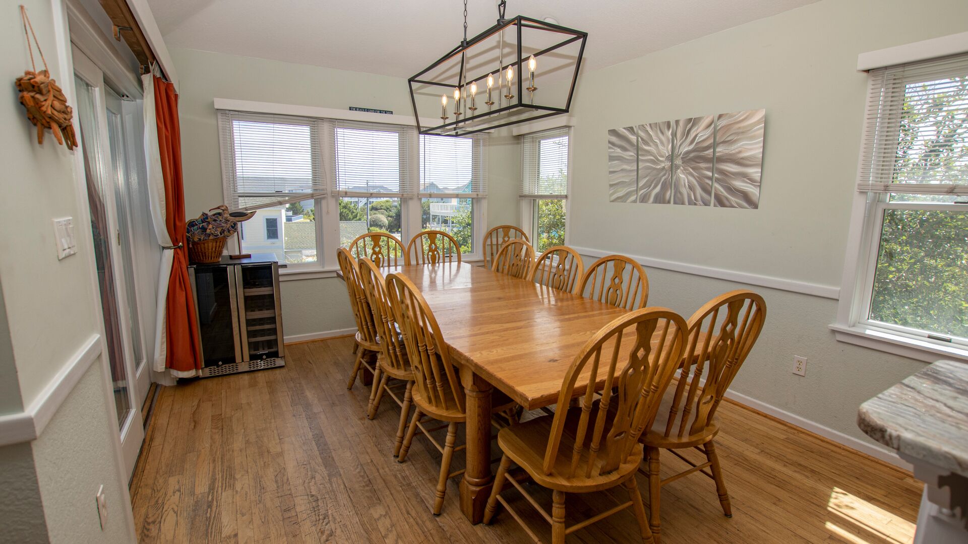 A dining room with a wooden table and chairs, large windows, and a modern chandelier.