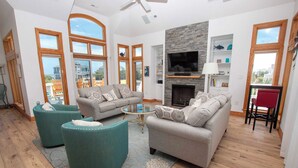 A spacious living area with a fireplace, comfortable seating, and large windows offering views of the outside. - Semi-Oceanfront, Close to Beach, Private Pool, Rec Room, PI13, Ocean's 13 (Corolla)