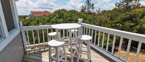 Eine Holzterrasse mit weißer Reling und einem kleinen Tisch mit zwei Stühlen.