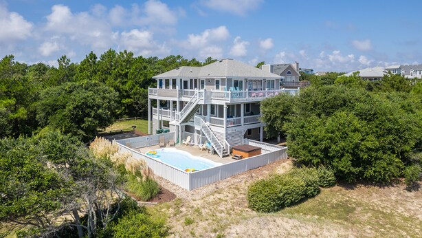 Uma casa de vários andares com piscina, rodeada por vegetação densa.