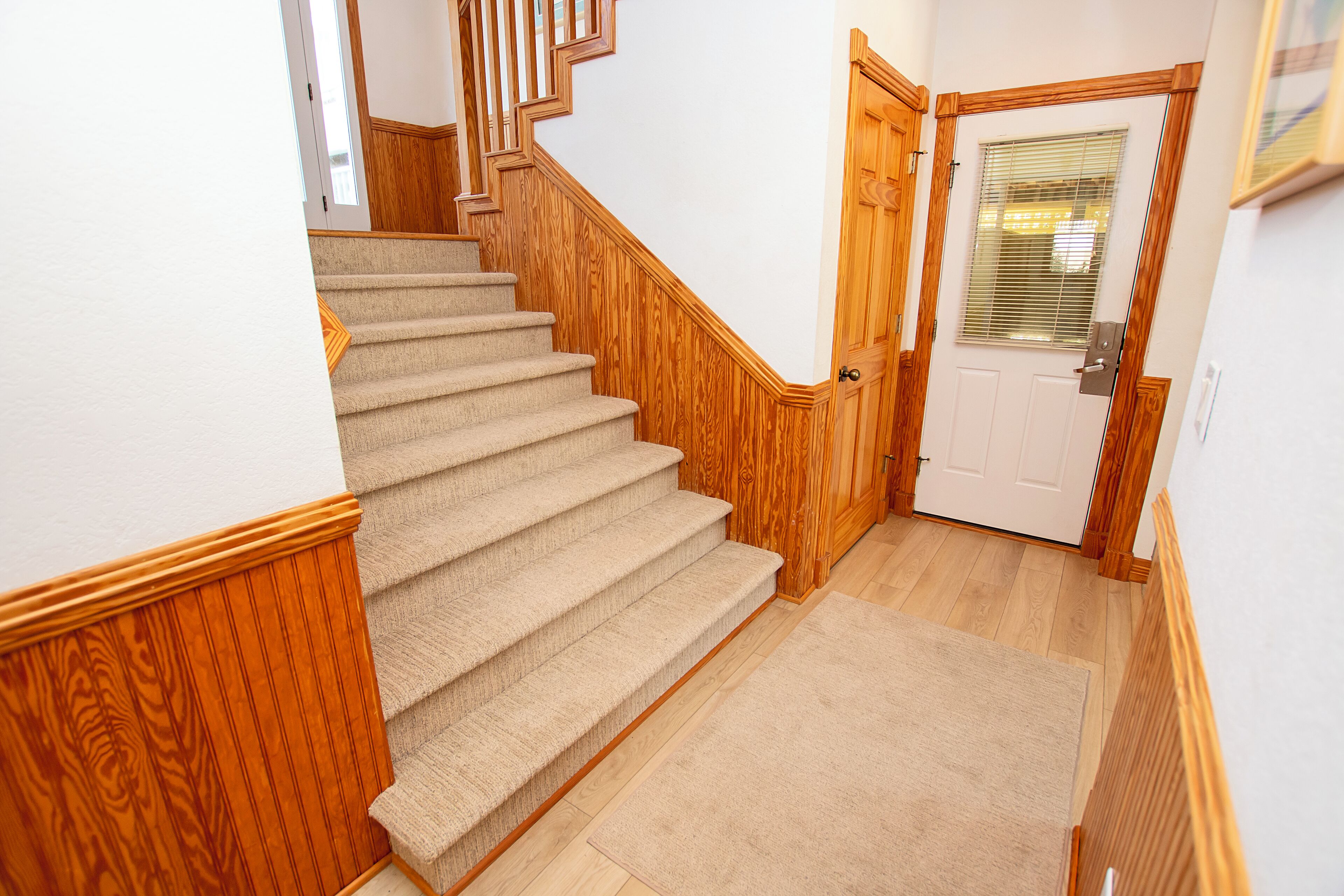 A carpeted staircase with wooden railings and a door with a window.