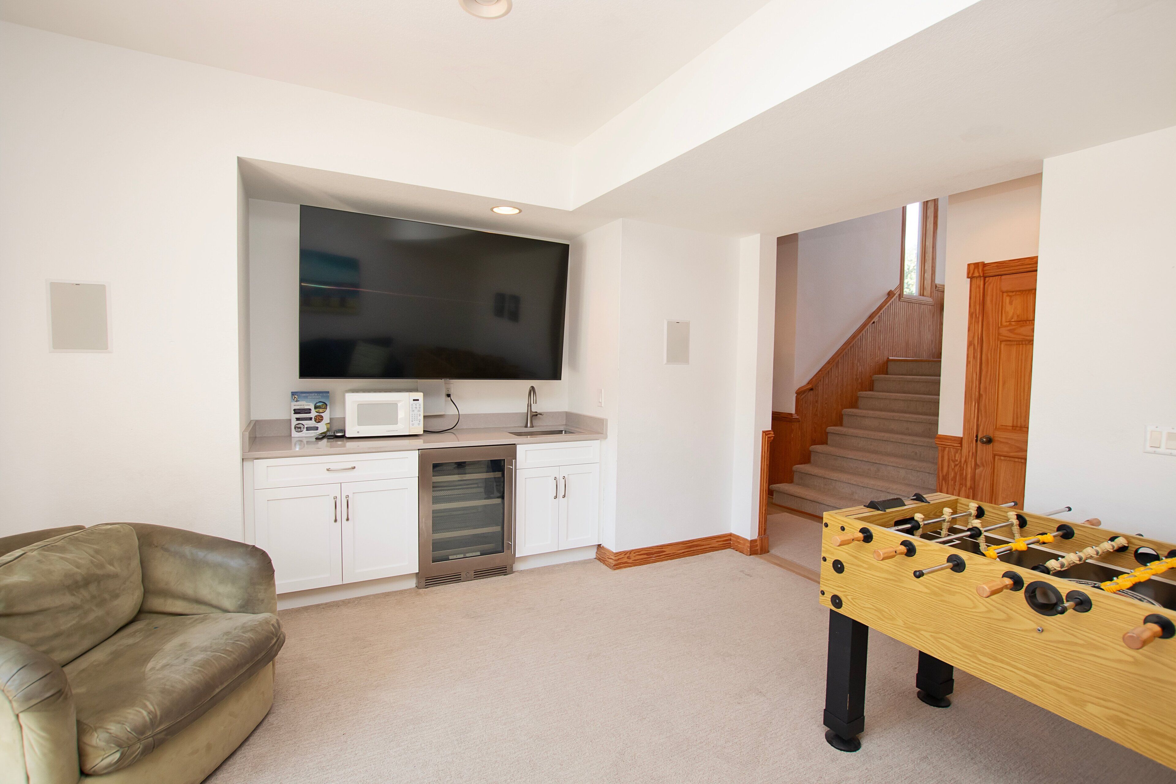 A living room with a foosball table, a sofa, a TV, and a kitchen area with a microwave.