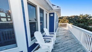 A wooden deck with white Adirondack chairs and a white railing.