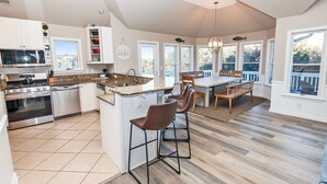A modern kitchen with a central island, bar stools, and a dining area with a view.