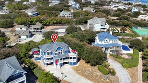 A coastal residential area with multiple houses, a prominent red location marker, and a view of the ocean.