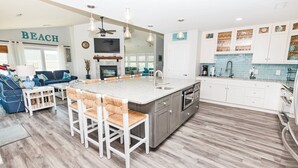 Eine moderne Küche mit einer großen Kochinsel, weißen Schränken und Blick auf das Wohnzimmer.