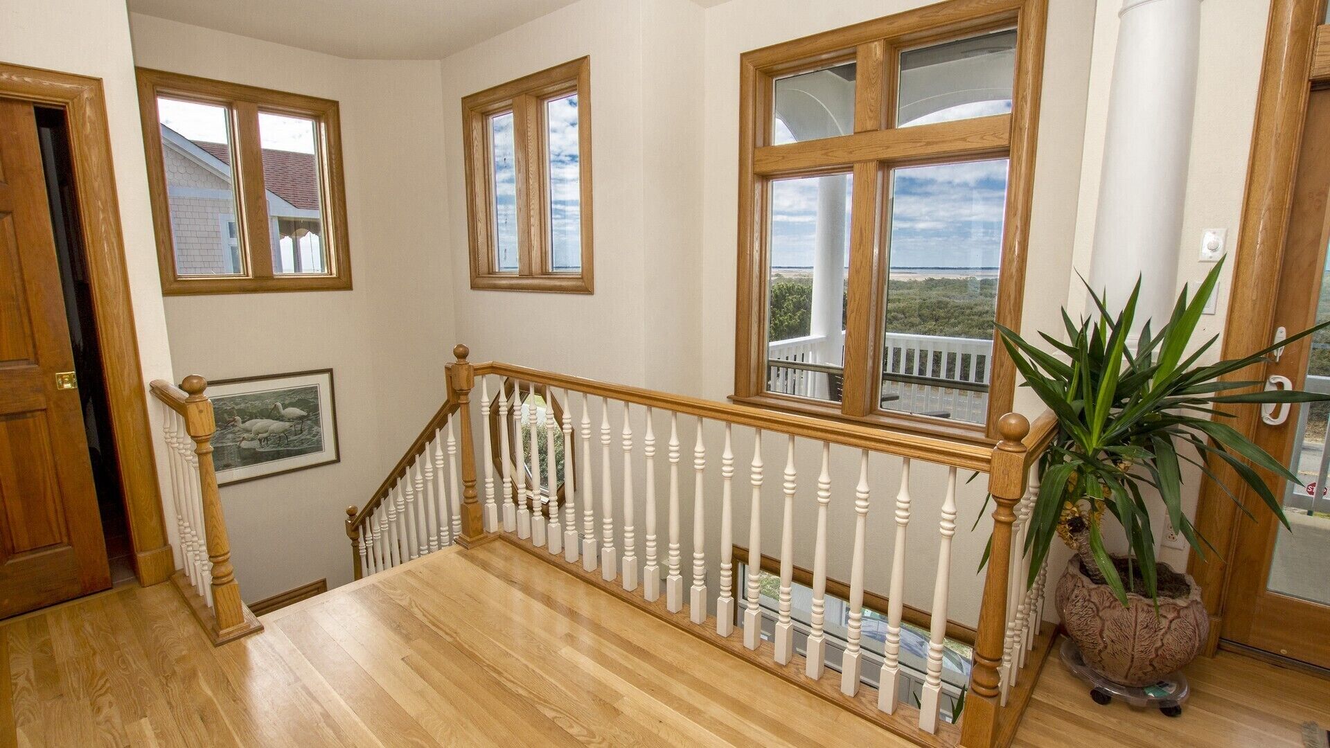 A staircase with a wooden railing, a potted plant, and a framed picture on the wall.