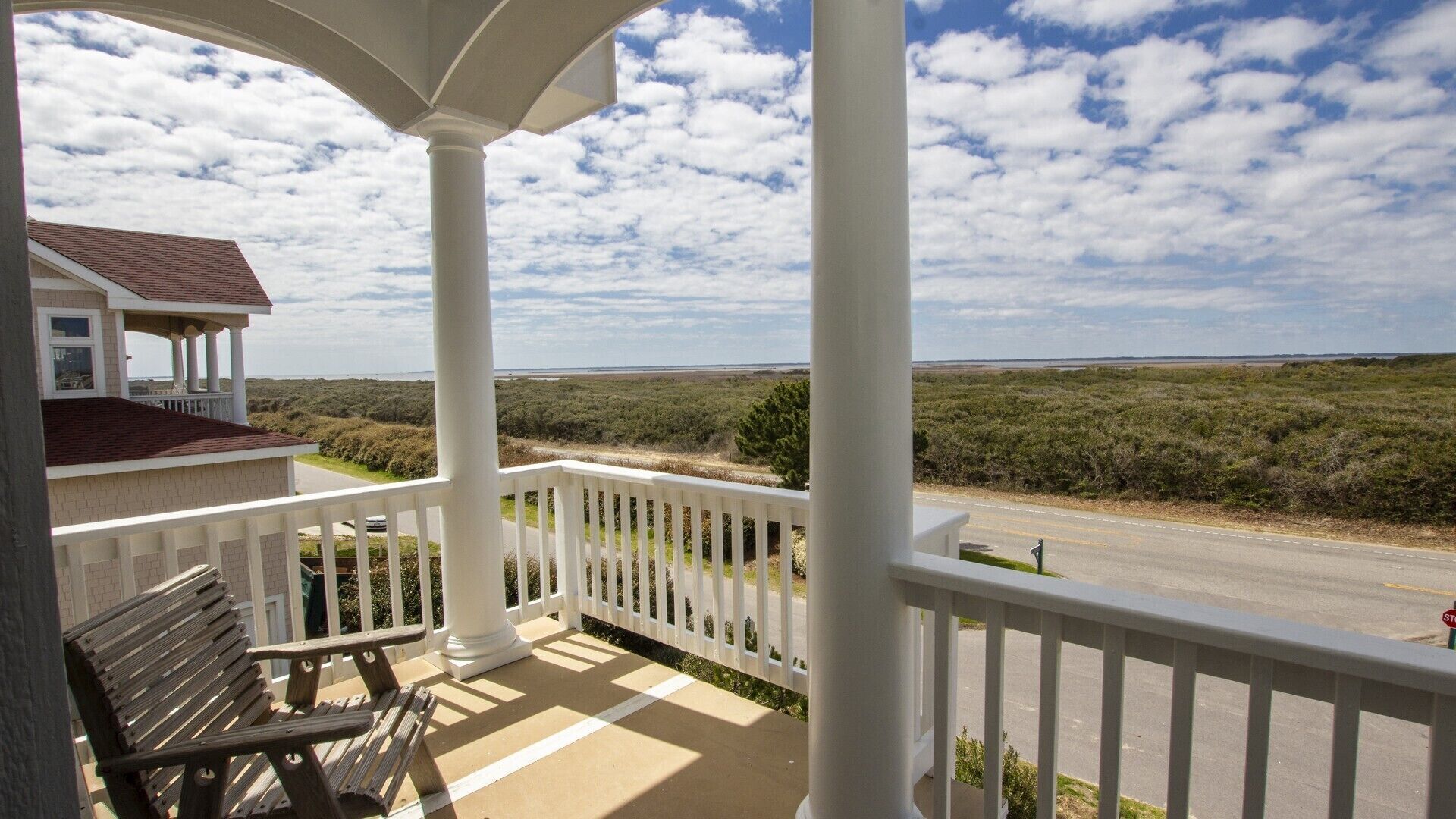 A porch with a bench, overlooking a road and a natural landscape.