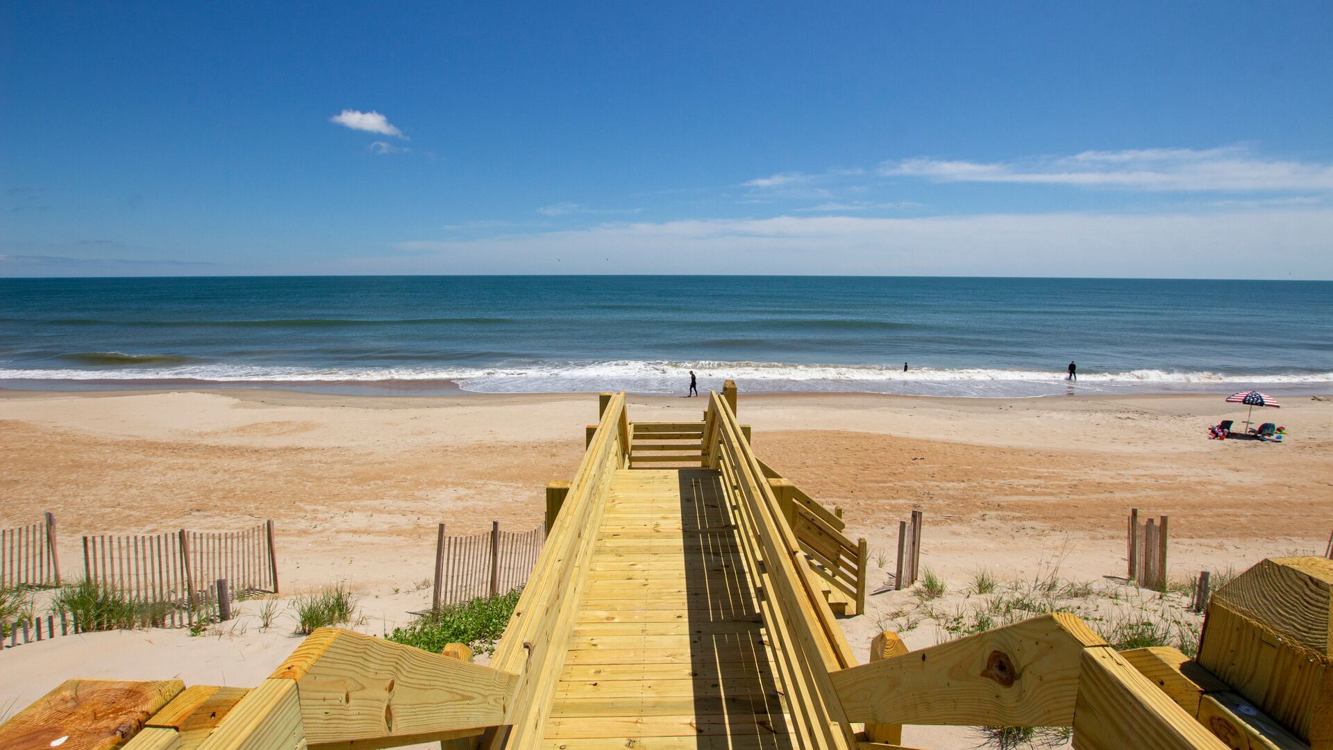 A wooden boardwalk leading to a sandy beach with the ocean in the background.