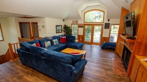 A spacious living room with a large sectional sofa, wooden flooring, and a television mounted on a wooden cabinet. - Semi-Soundfront, Private Pool, Hot Tub, Community Amenities, 507, N-2-Wishn (Corolla)