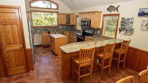 A kitchen with wooden cabinets, granite countertops, a central island with bar stools, a refrigerator, an oven, and a microwave. - Semi-Soundfront, Private Pool, Hot Tub, Community Amenities, 507, N-2-Wishn (Corolla)