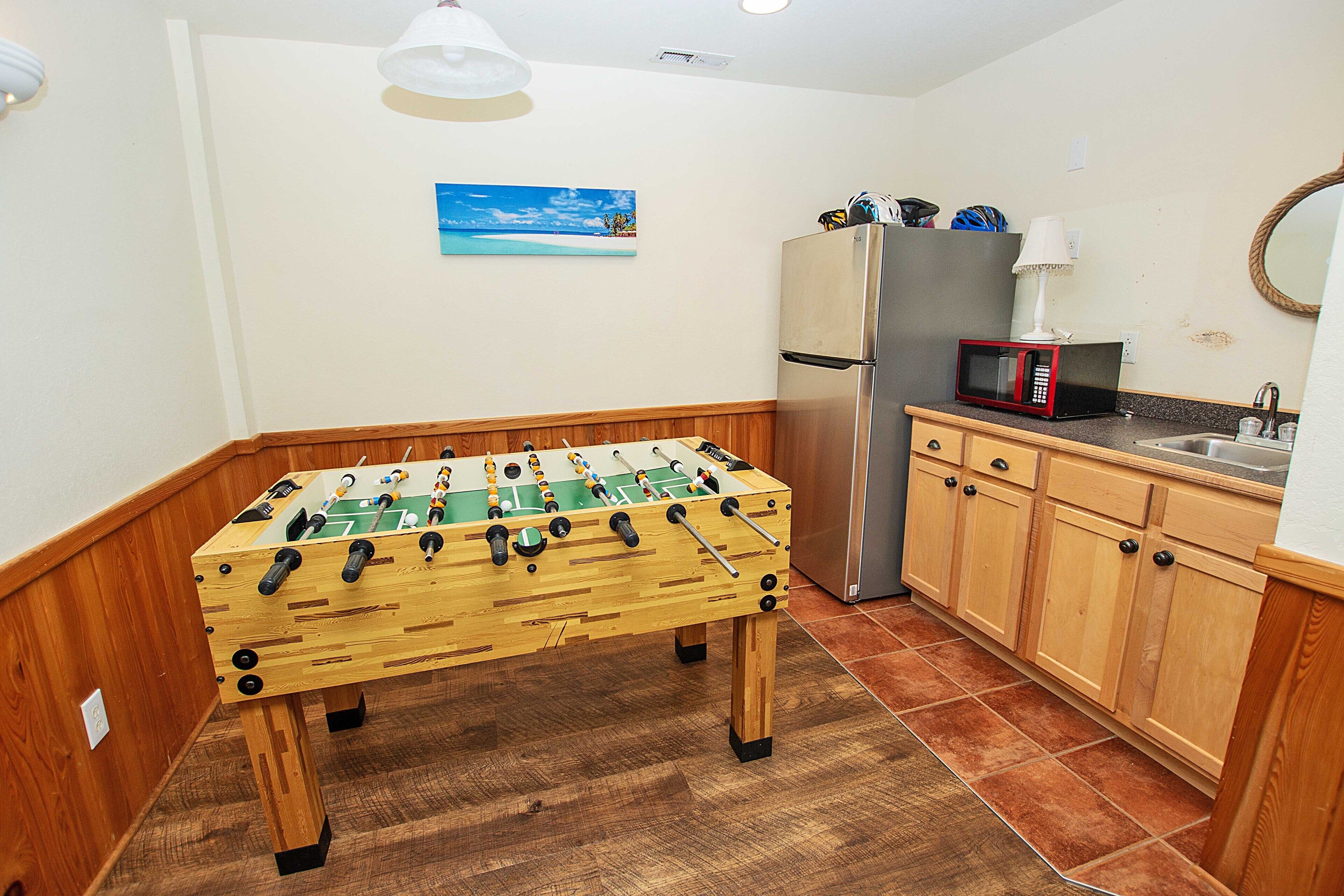 A kitchen with wooden cabinets, a foosball table, a refrigerator, and a microwave.