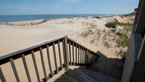 En trætrap fører ned til en sandstrand med udsigt over havet.