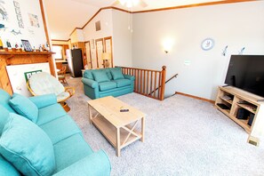 A living room with a teal sofa, a wooden coffee table, and a television on a wooden stand. - Oceanside, Close to Beach Access, Community Pool, Ocean Views, KHSDC2, Sea Dunes C2 (Kitty Hawk)