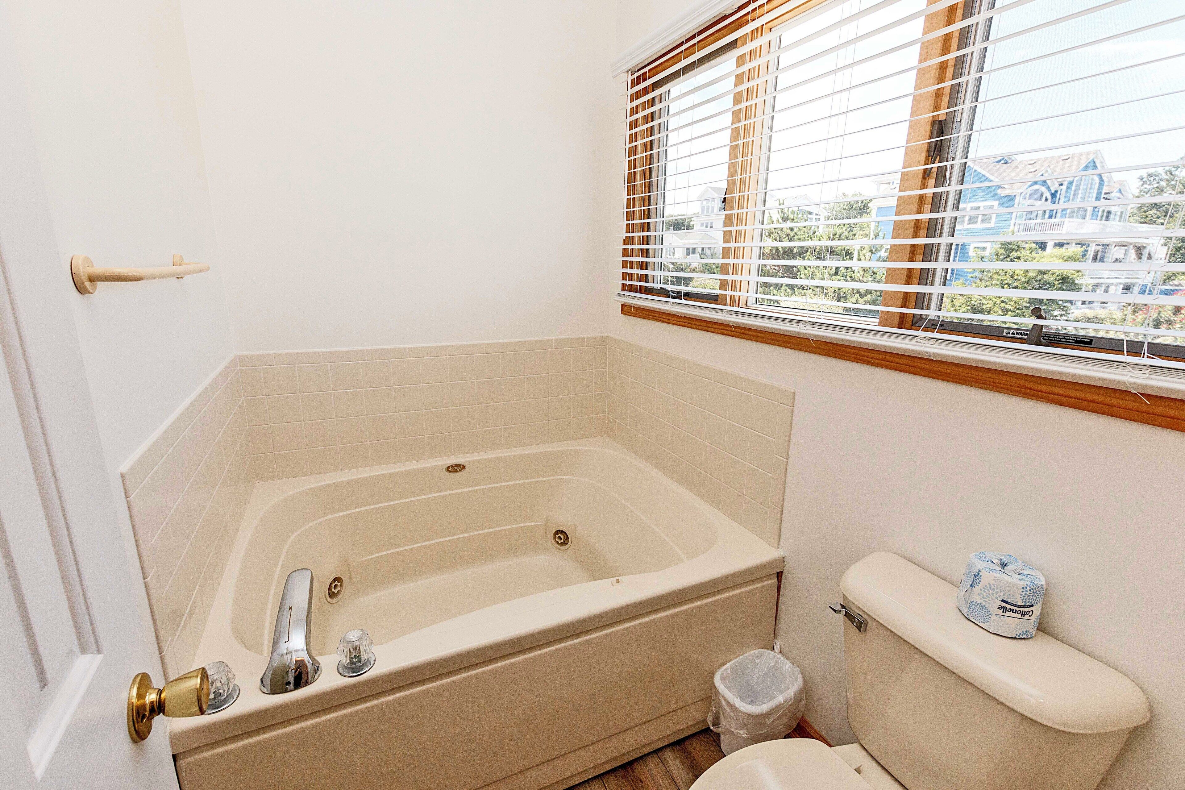 A bathroom with a bathtub, toilet, and window with blinds.