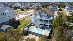 Une grande maison à deux étages dotée d’une piscine, de plusieurs balcons et d’une pelouse bien entretenue.