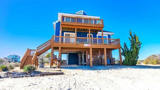 A two-story beachfront house with a wooden deck and a staircase leading to the entrance. - Semi-Oceanfront, Pets Welcome, Wild Horses, Ocean Views! 4x1678, Turtle Trax (Corolla)
