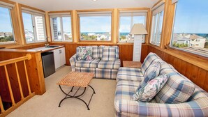 A cozy room with a kitchenette, a sofa set, and large windows offering a view of the sea and neighboring houses. - Oceanside, Priv Pool, poolside grilling, sun decks, SEA6, Morningstar (Duck)