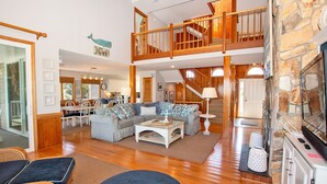 A spacious living area with a high ceiling, wooden staircase, and a stone fireplace. - Oceanside, Priv Pool, poolside grilling, sun decks, SEA6, Morningstar (Duck)