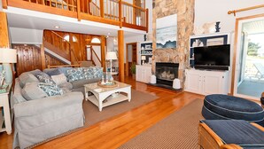 A spacious living room with a high ceiling, wooden staircase, and a fireplace. - Oceanside, Priv Pool, poolside grilling, sun decks, SEA6, Morningstar (Duck)