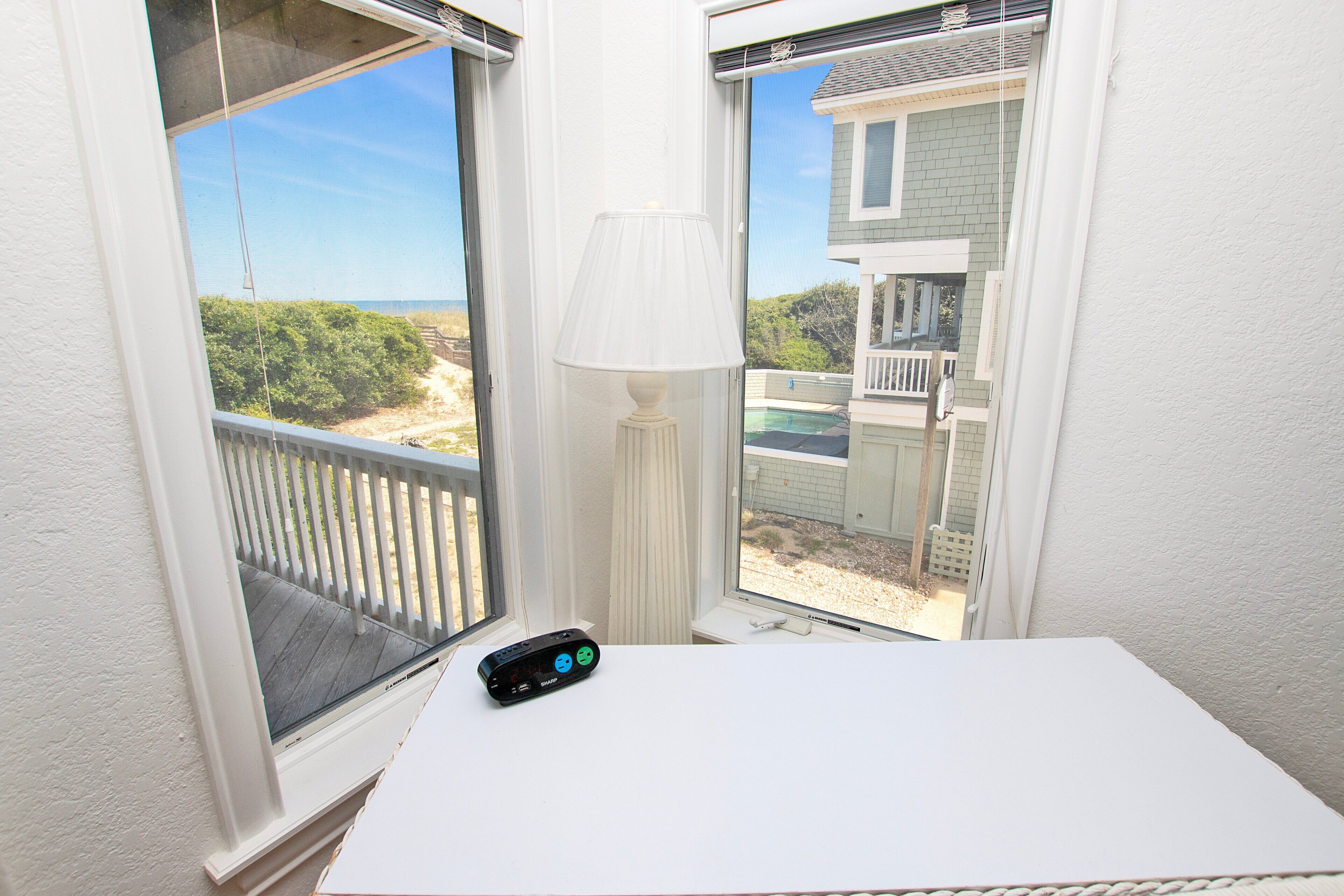 A room with a view of a beach, a white table, and a lamp.