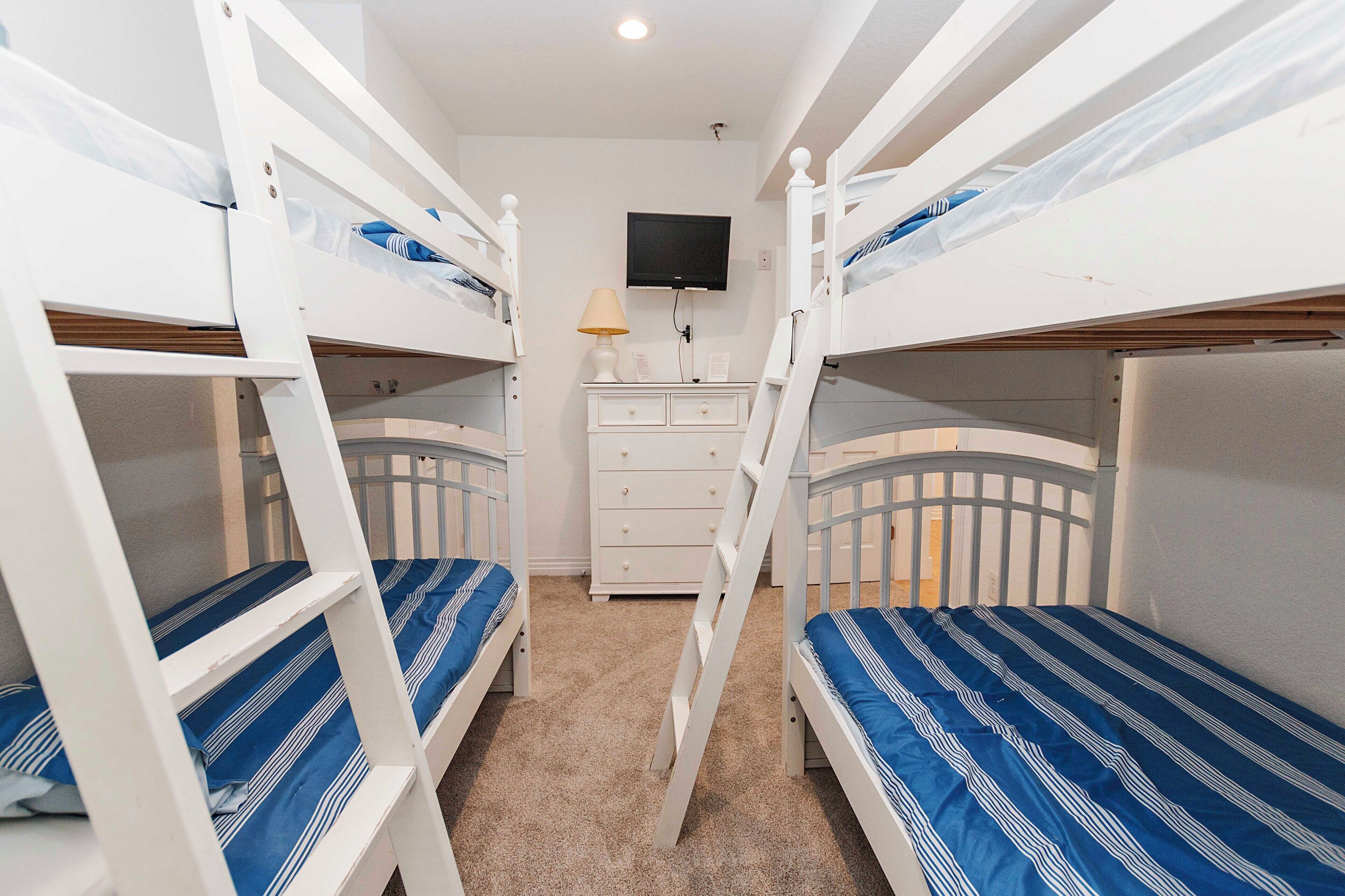A bunk bed room with a TV mounted on the wall, a dresser, and a ladder.