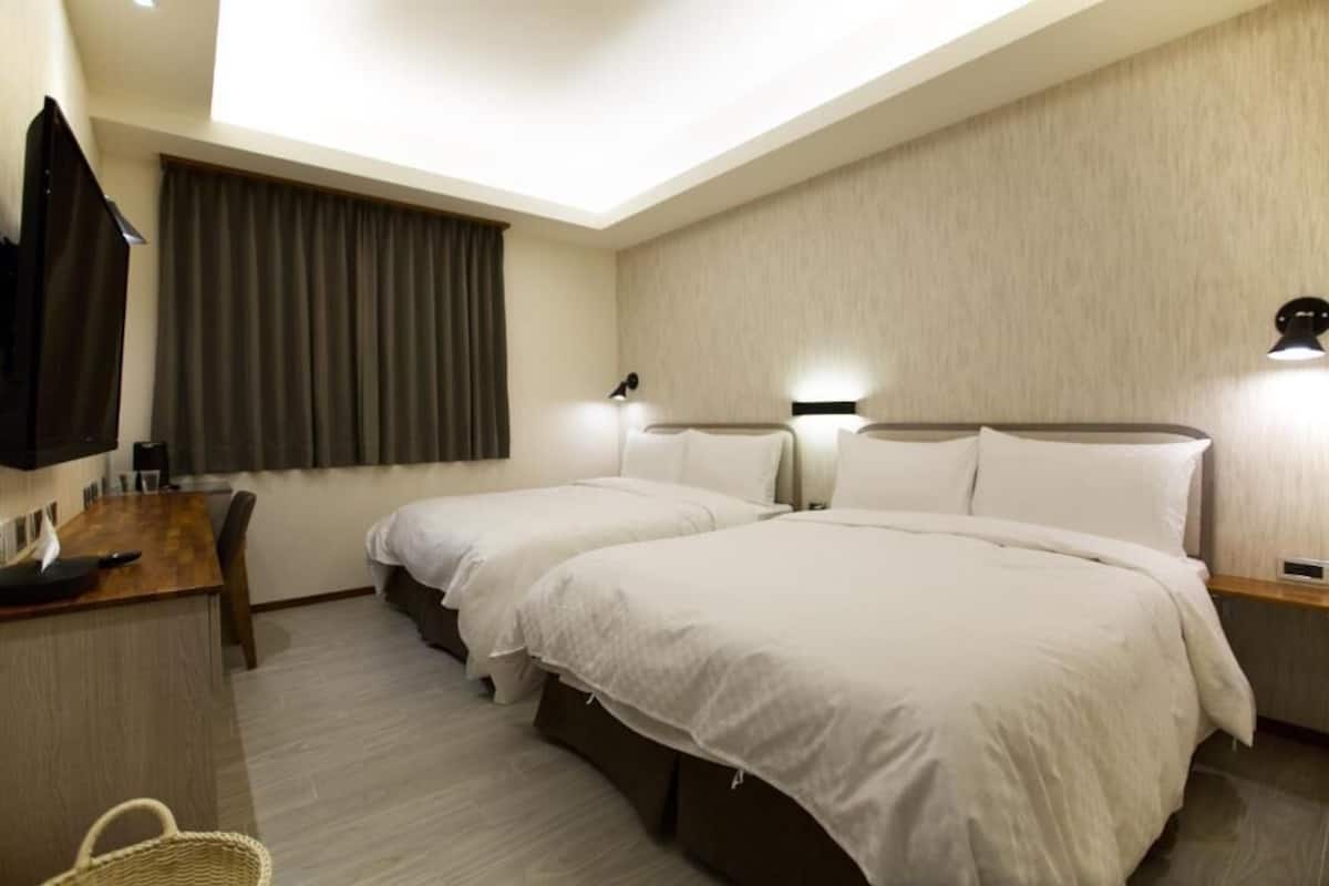 A hotel room with two beds, a desk with a chair, a TV, and a window with curtains.