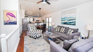 A modern living room with a gray sofa, patterned armchair, and a coffee table. A ceiling fan is visible, and there are two paintings on the walls. - Oceanside, Close to Beach Access, Community Pool, KHSDD1, Sea Dunes D1 (Kitty Hawk)