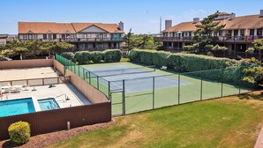 A tennis court surrounded by a fence, a pool, and a building with balconies. - Oceanside, Close to Beach Access, Community Pool, KHSDD1, Sea Dunes D1 (Kitty Hawk)