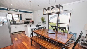 A modern kitchen with white cabinets, a wooden dining table, and a built-in island with a sink. - Oceanside, Close to Beach Access, Community Pool, KHSDD1, Sea Dunes D1 (Kitty Hawk)