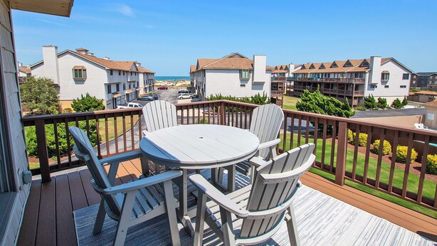 A balcony with a round table and chairs, overlooking a beachfront community with multiple-story buildings. - Oceanside, Close to Beach Access, Community Pool, KHSDD1, Sea Dunes D1 (Kitty Hawk)