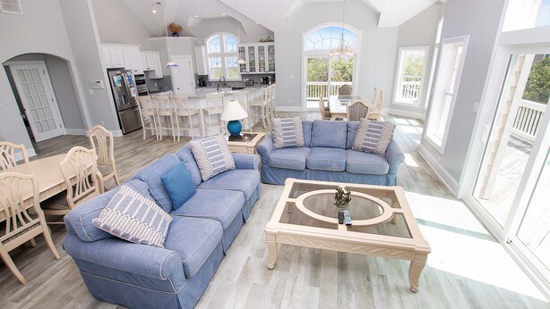 A spacious living area with a blue sofa set, a coffee table, and a dining table with chairs.