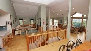 A spacious living area with a wooden staircase, a dining area with a table and chairs, and a kitchen visible in the background.