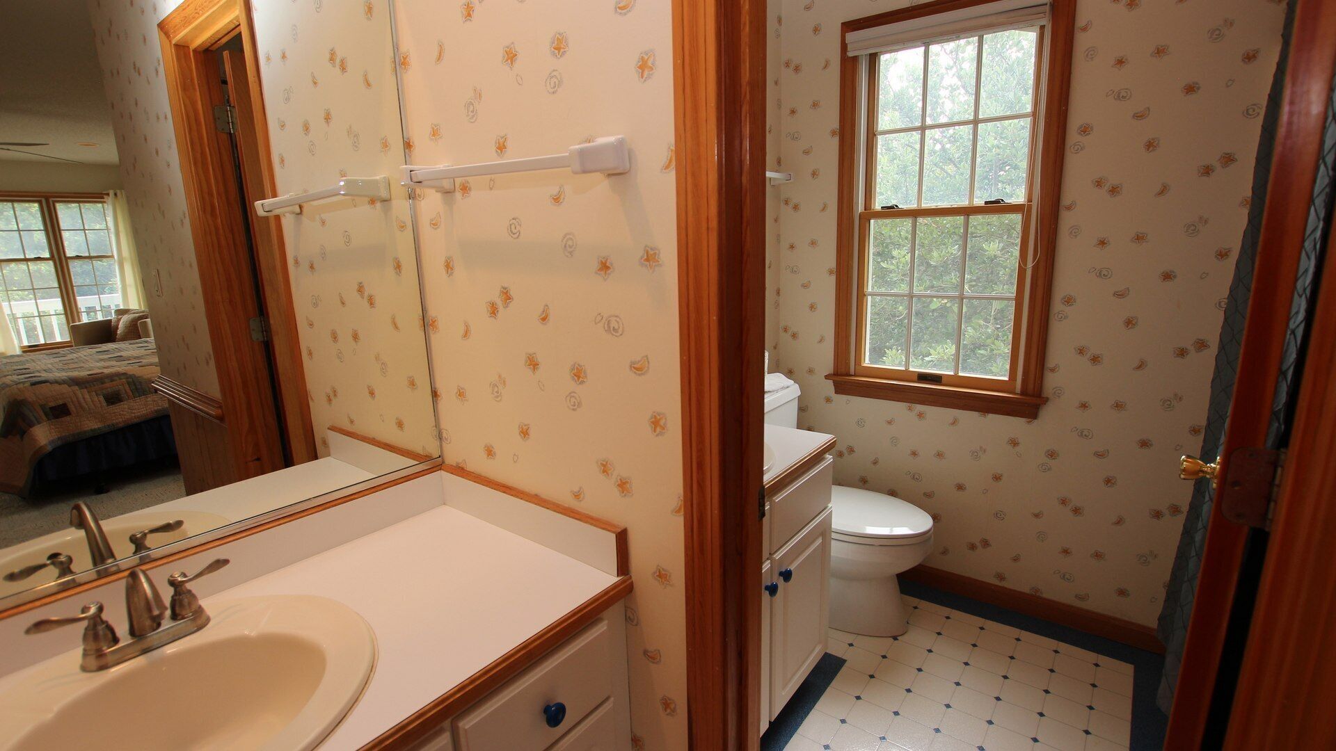 A bathroom with a toilet, sink, and mirror. There is a window above the toilet and a door leading to another room.