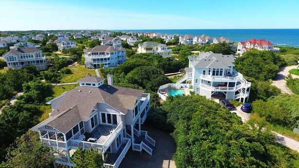 A coastal residential area with multiple two-story houses featuring large balconies, a swimming pool, and a view of the ocean.