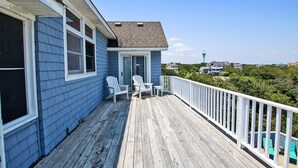 A wooden deck with two white Adirondack chairs and a small table, overlooking a residential area with houses and trees. - Oceanside, Private Pool, Volleyball, Screened porch, PI61, Without a Porpoise (Corolla)