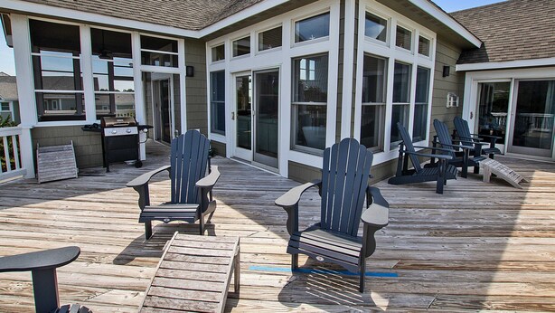 Eine Terrasse mit Adirondack-Stühlen, einem Tisch, großen Fenstern und einem überdachten Bereich.