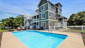 Ein zweistöckiges Haus mit Swimmingpool, Gartenmöbeln und einem umzäunten Deck.