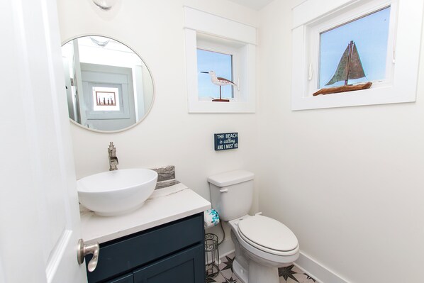 A bathroom with a white sink, a toilet, a mirror, and a small window with a sailboat decoration. - Semi-Oceanfront, Wild Horses, Hot Tub, Ocean Views! 4x2000, Sandfiddler Inn (Corolla)