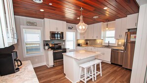 A modern kitchen with wooden flooring, white cabinetry, a central island with stools, a stainless steel refrigerator, and a coffee machine.