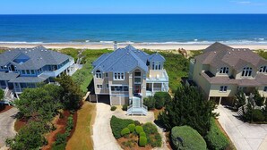 A coastal residential area with houses featuring gabled roofs and a prominent central house with a front porch and steps leading to the entrance. - OCEANFRONT, Ocean views, beach access, Pool, PI139, Pine Haven (Corolla)